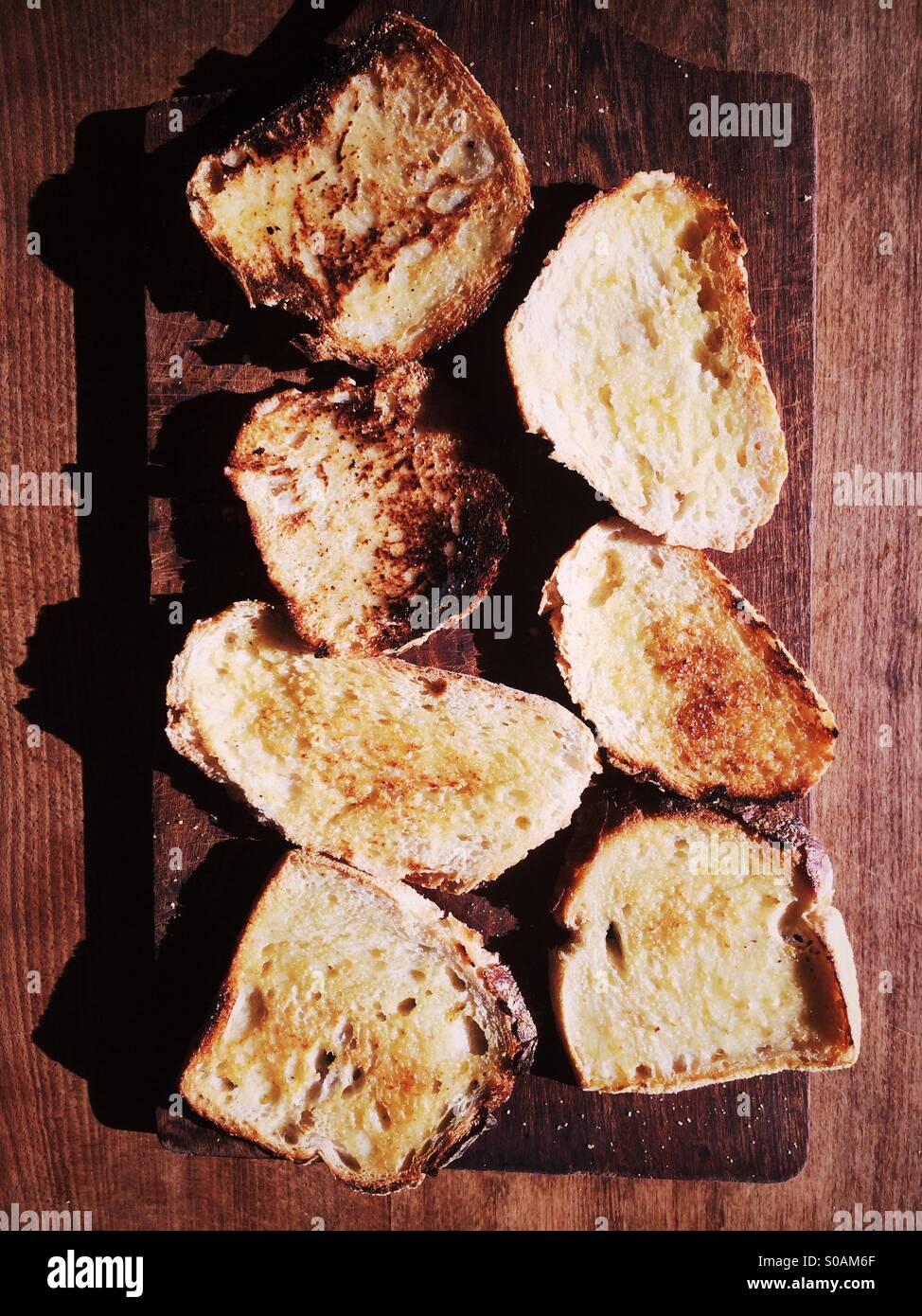 Fette di pasta madre imburrato toast su un tagliere di legno. Foto Stock