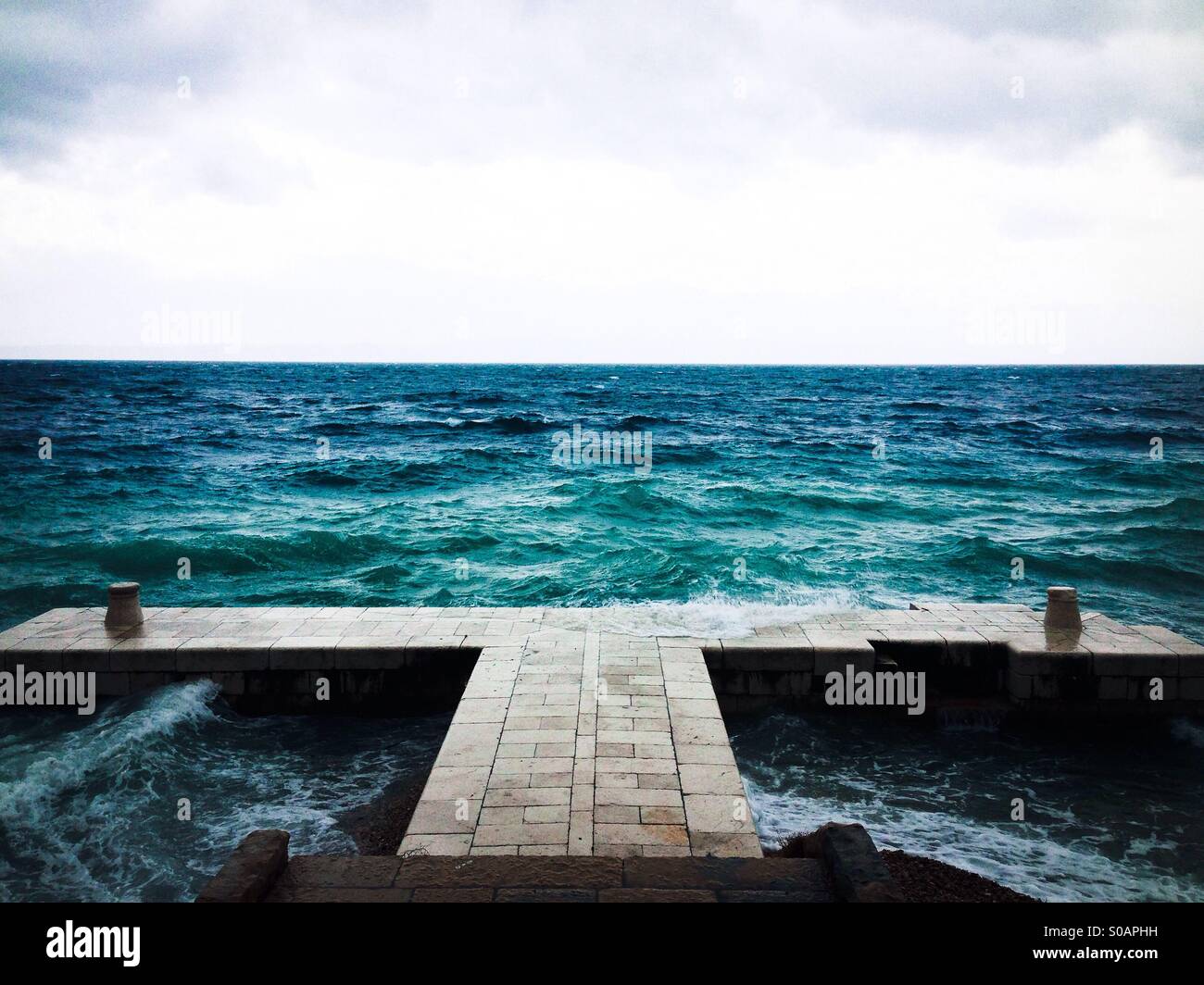 Il molo di pietra e le onde nel mare sullo sfondo Foto Stock
