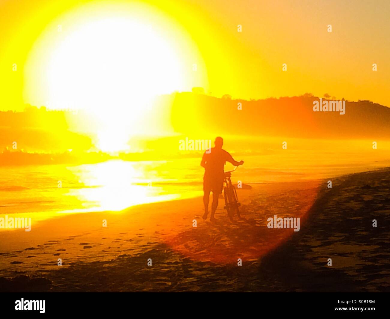 L'uomo cammina la sua bicicletta lungo una spiaggia in California al tramonto Foto Stock