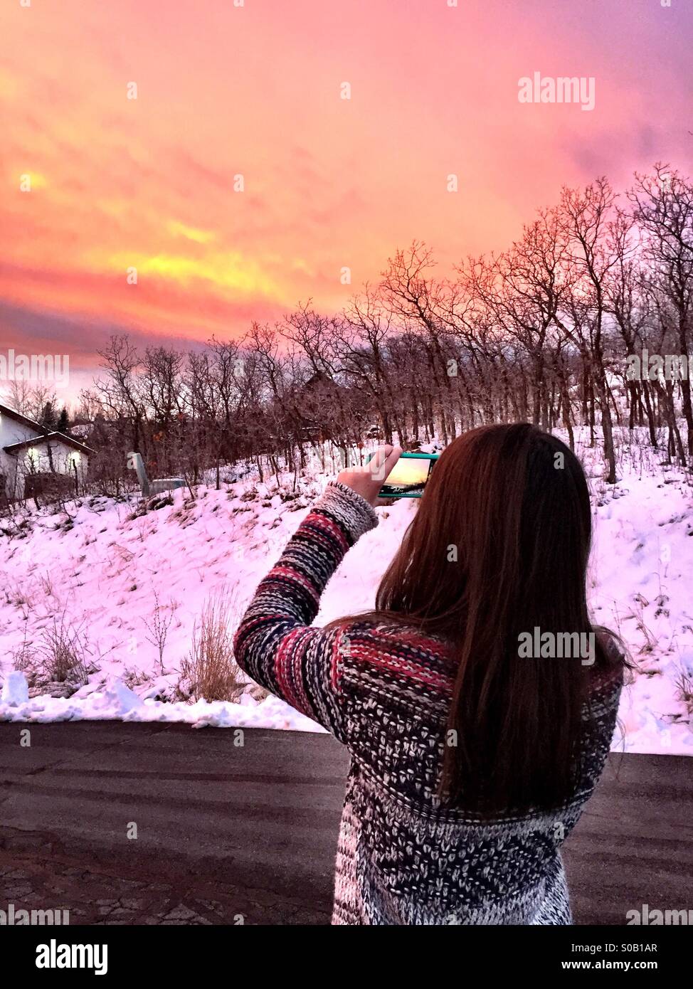 Una ragazza adolescente prende le foto del tramonto usando il suo iPhone. Foto Stock