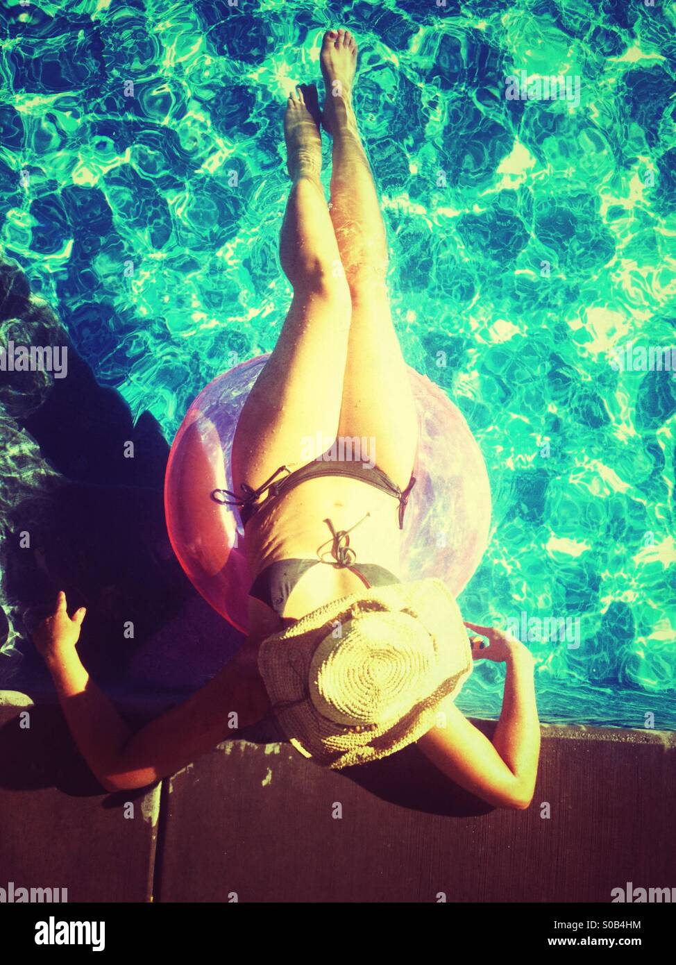 Donna che indossa hat oziare in piscina, crogiolandosi al sole. Foto Stock