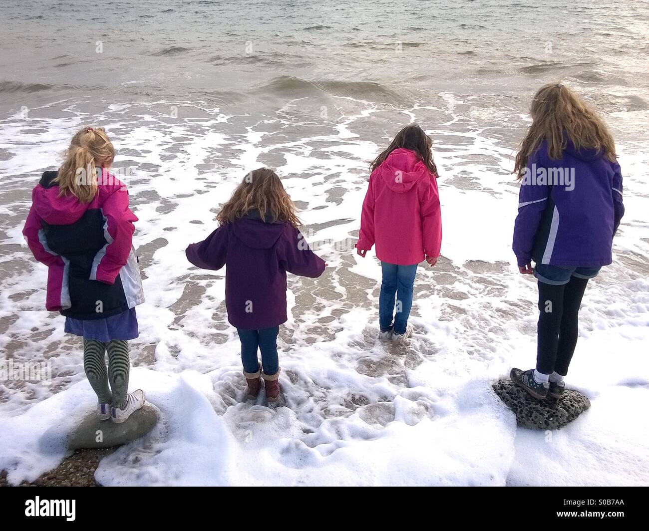 Le quattro ragazze in equilibrio su pietre a lavare alla spiaggia. Foto Stock