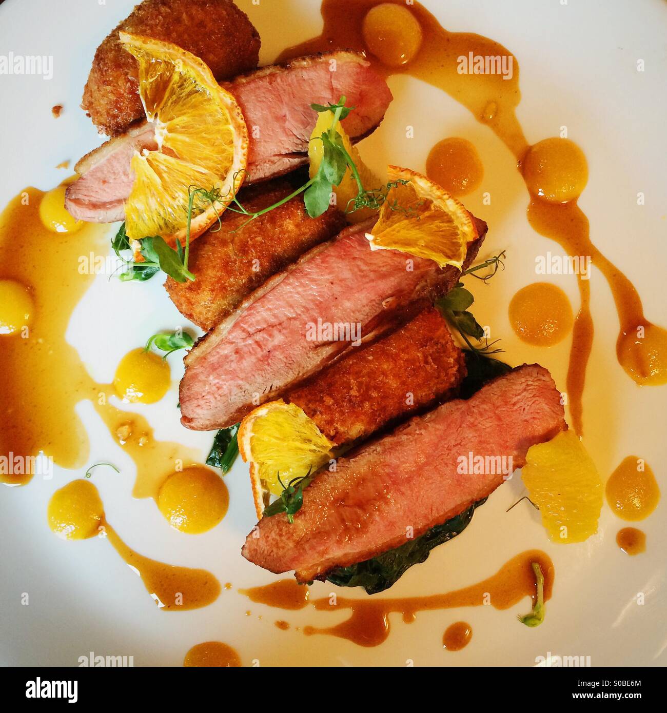 Duck a l'arancione, Bacon & Anatra confit leg crocchette, appassì spinaci, arancione jus Foto Stock