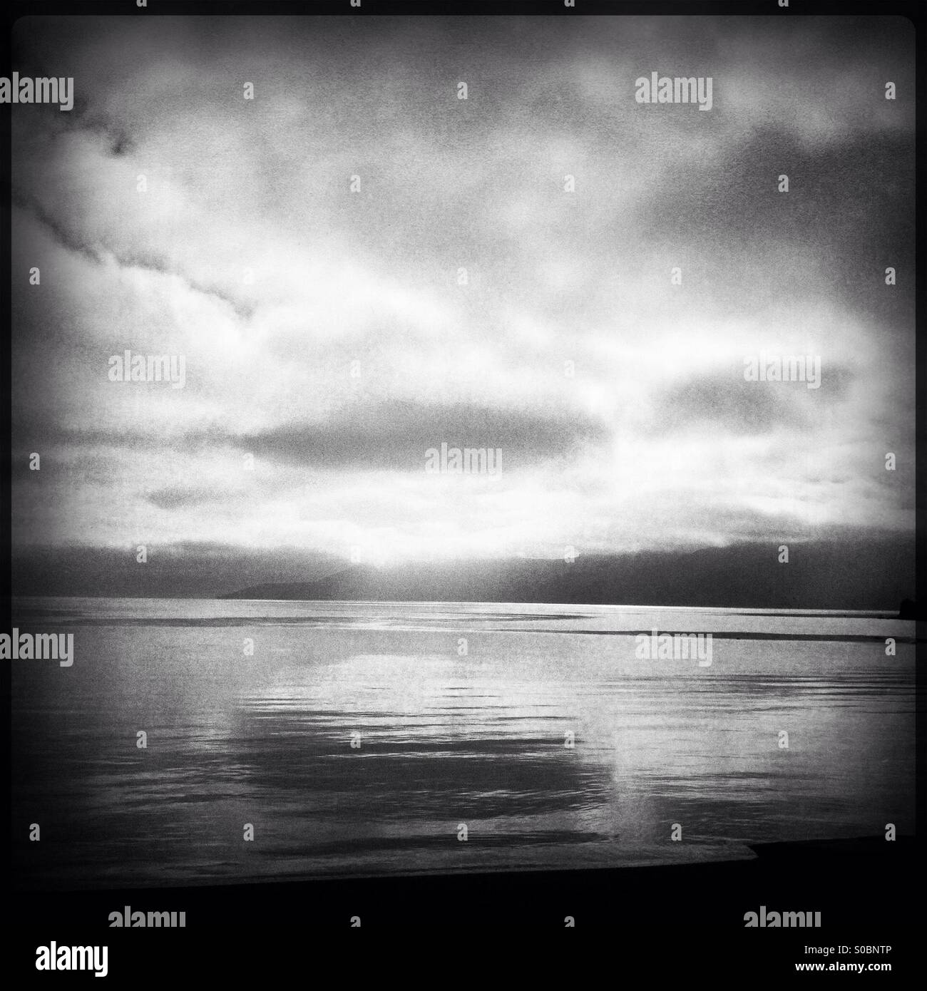 Soleggiato nuvole riflettono ancora, vitreo mare. Promontorio distante - Immagine stock catturata con smartphone