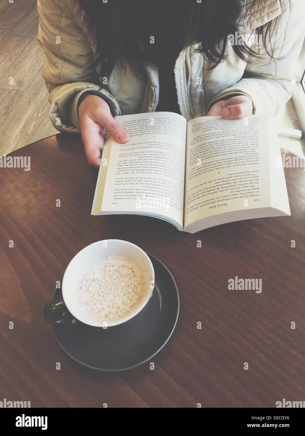 Ragazza la lettura di un libro in una caffetteria. Tazza di caffè e prenota Foto Stock