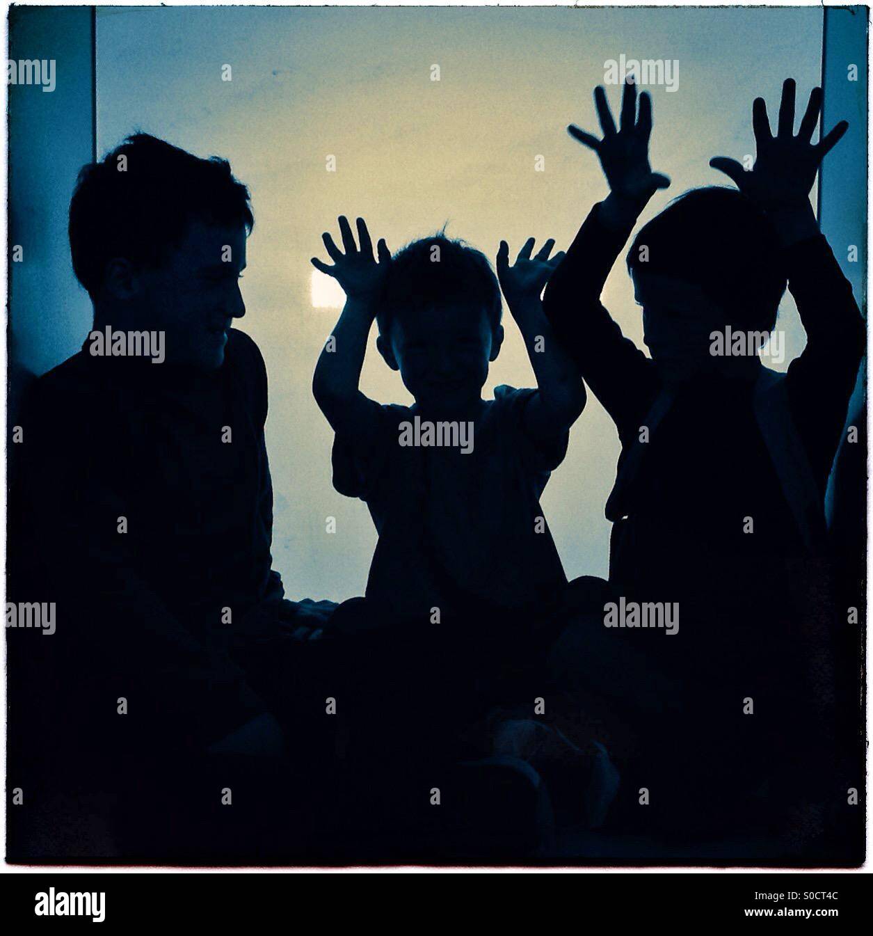 Tre bambini sagome a giocare con le mani in alto Foto Stock