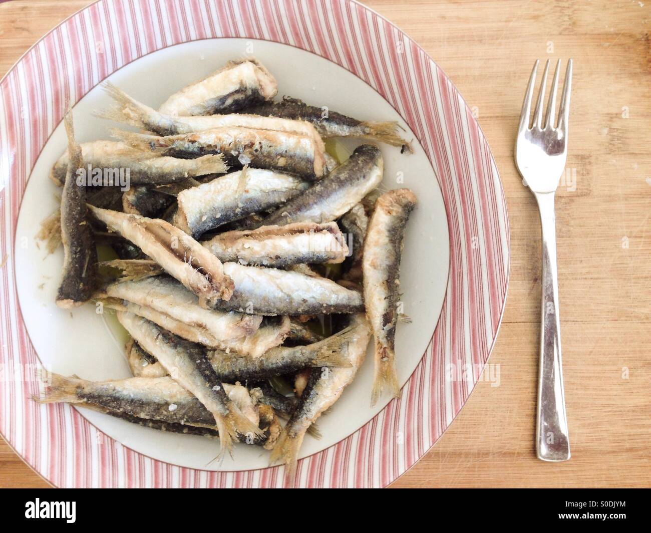 Le sardine fritte nella ciotola con forcella sullo sfondo di legno Foto Stock