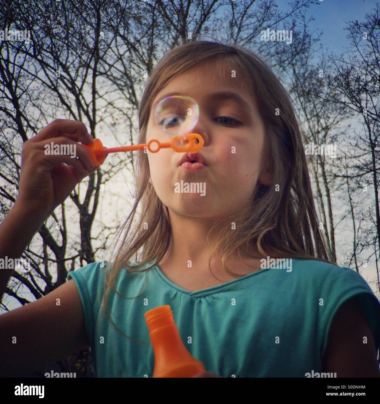 Ragazza soffia una bolla con una bacchetta di bolle Foto Stock