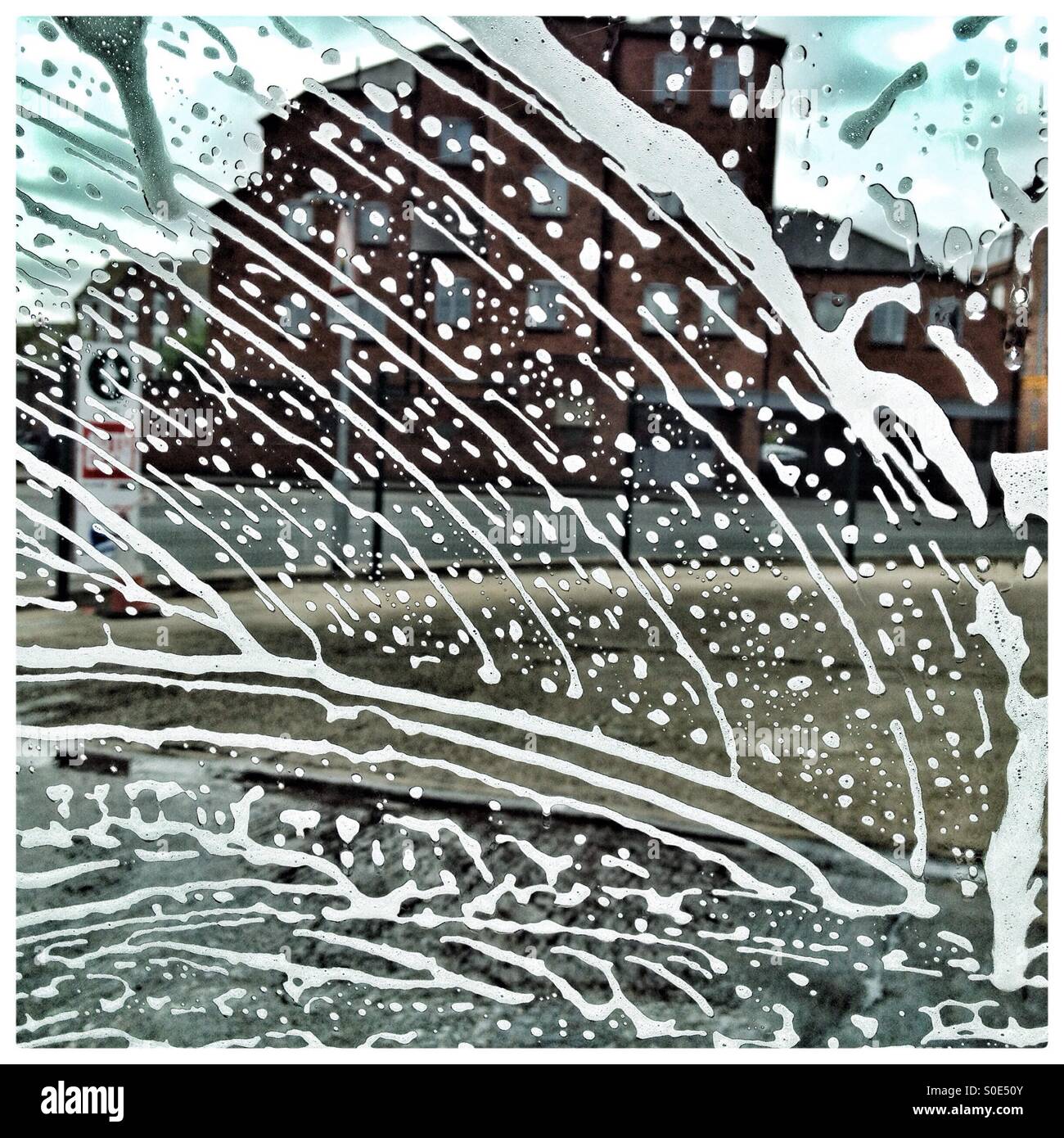 Al carwash; sapone liquido formano una configurazione astratta su di un parabrezza di automobile, scattato dall'interno dell'auto. - Immagine stock catturata con smartphone