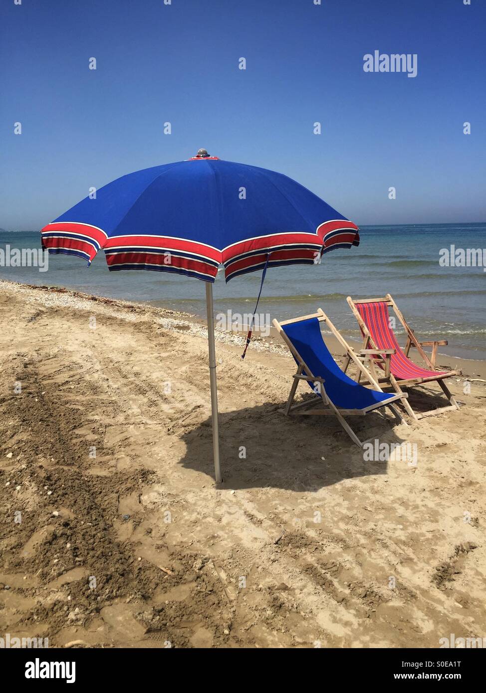 Primo sole sulla spiaggia, vista su un ombrellone e due sdraio durante una giornata di primavera - Immagine stock catturata con smartphone