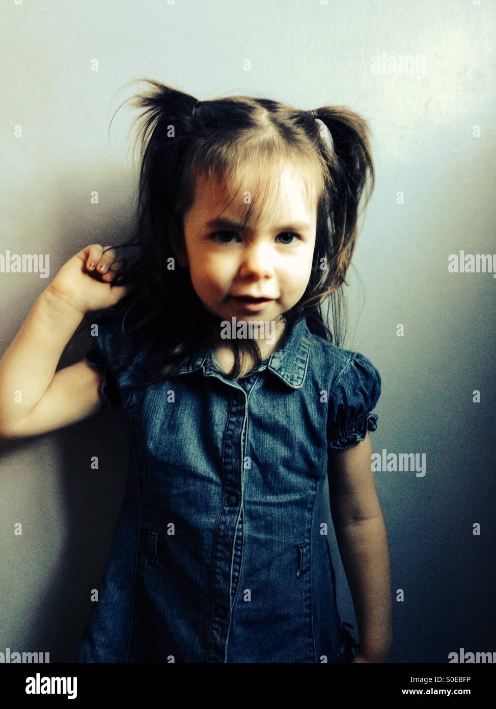 3 anno vecchia ragazza in abito di denim e pigtail nei suoi capelli Foto Stock