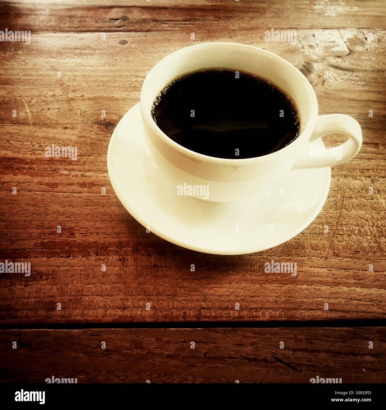 Una tazza di caffè nero in una tazza bianca e il piattino è collocato su un tavolo di legno pronto per essere gustato. Foto Stock
