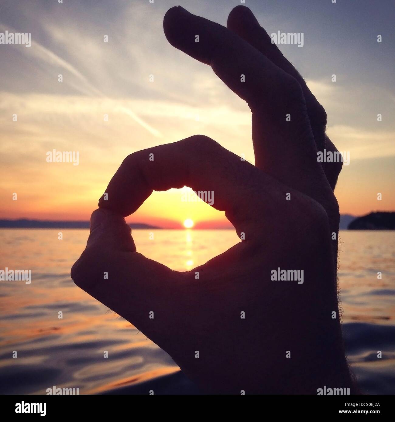 Man mano intorno al sole nel tramonto sul mare Foto Stock