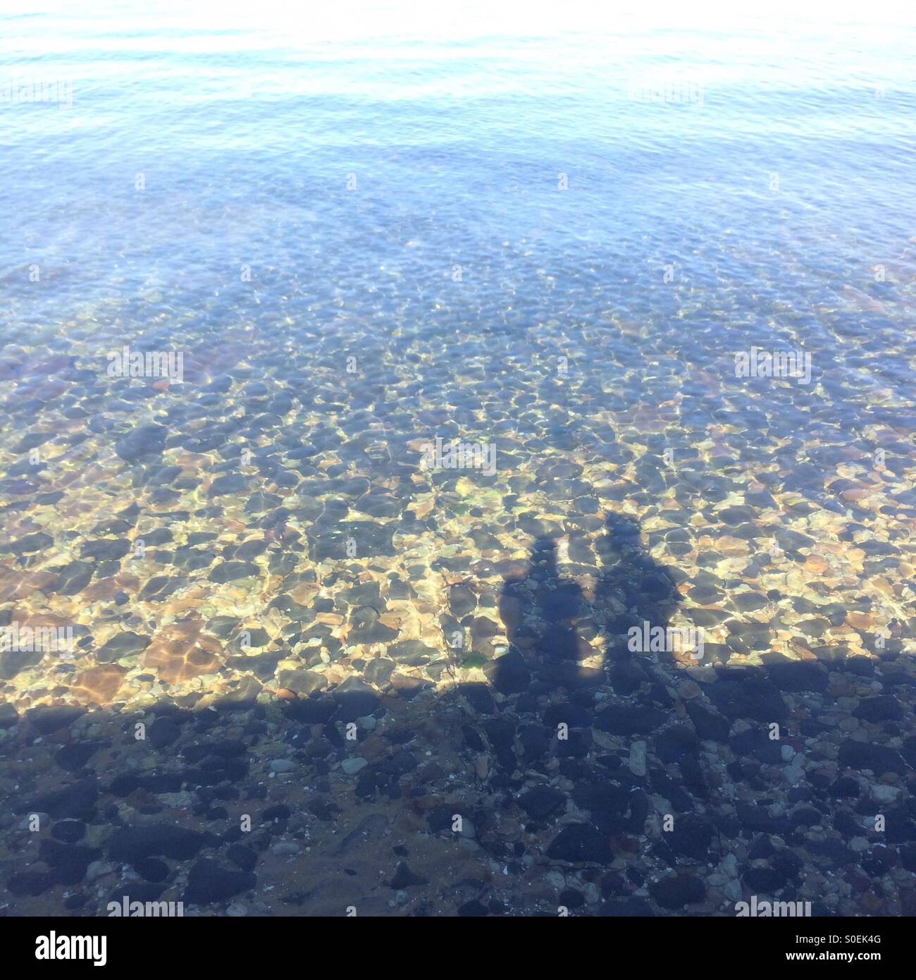 Le ombre di due persone in piedi che guarda sul mare, con rocce sotto l'acqua Foto Stock