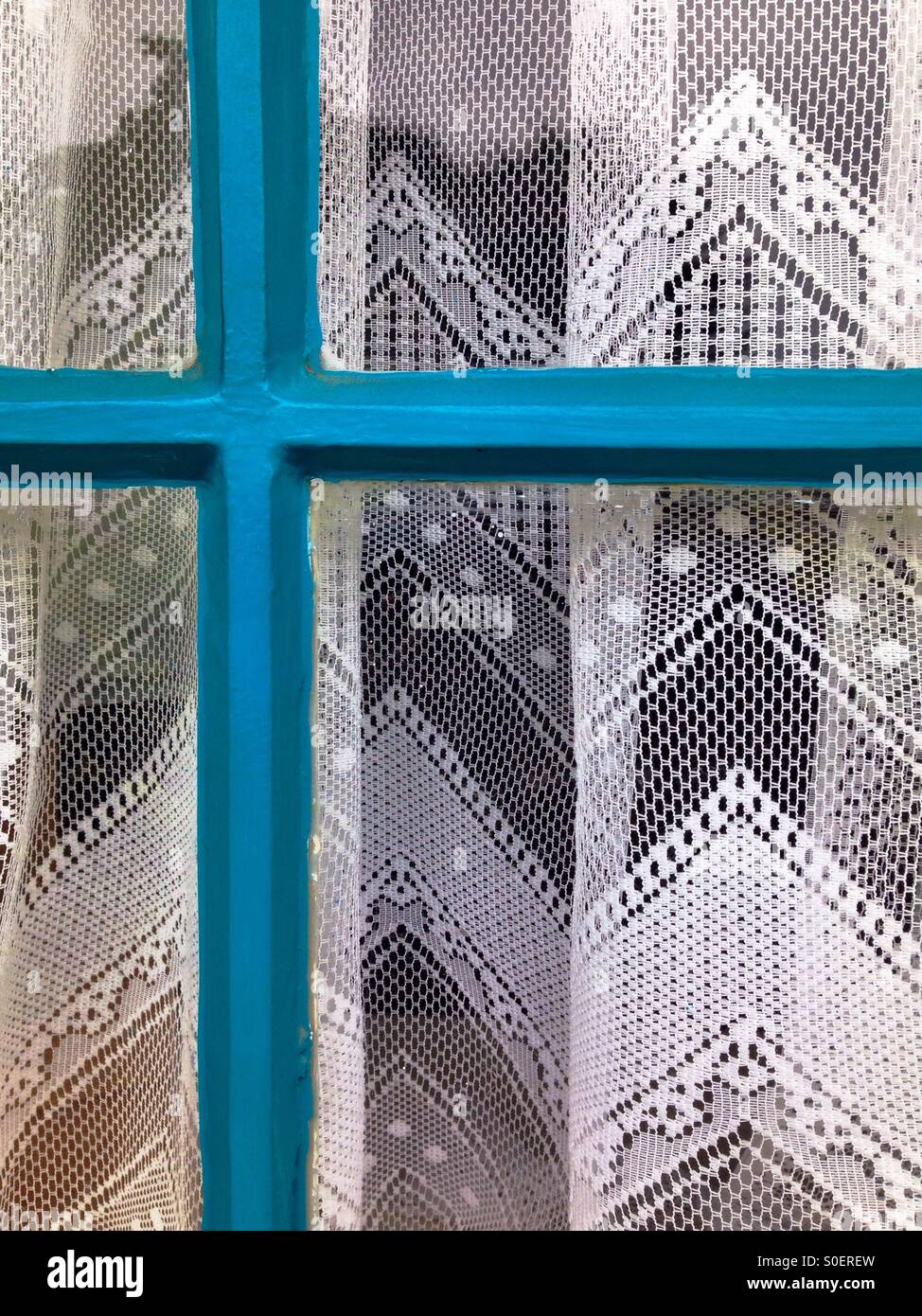 La tendina di pizzo dietro il blu sul telaio di una finestra Foto Stock