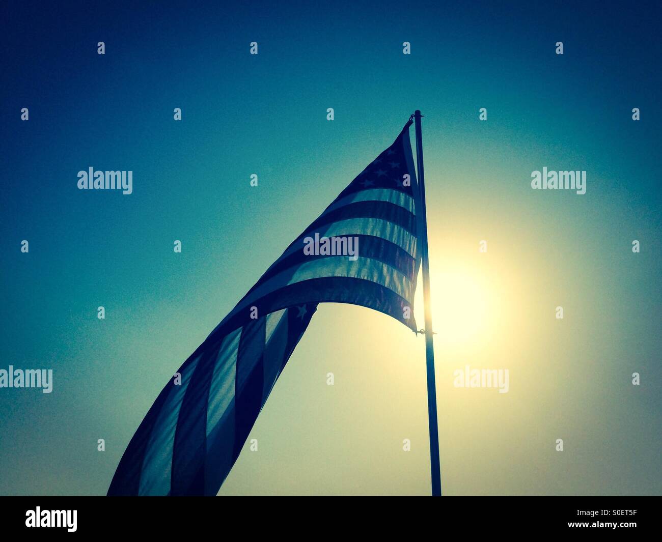 Bandiera americana al di fuori su di un pennone con il sole di mattina dietro di essa - Immagine stock catturata con smartphone