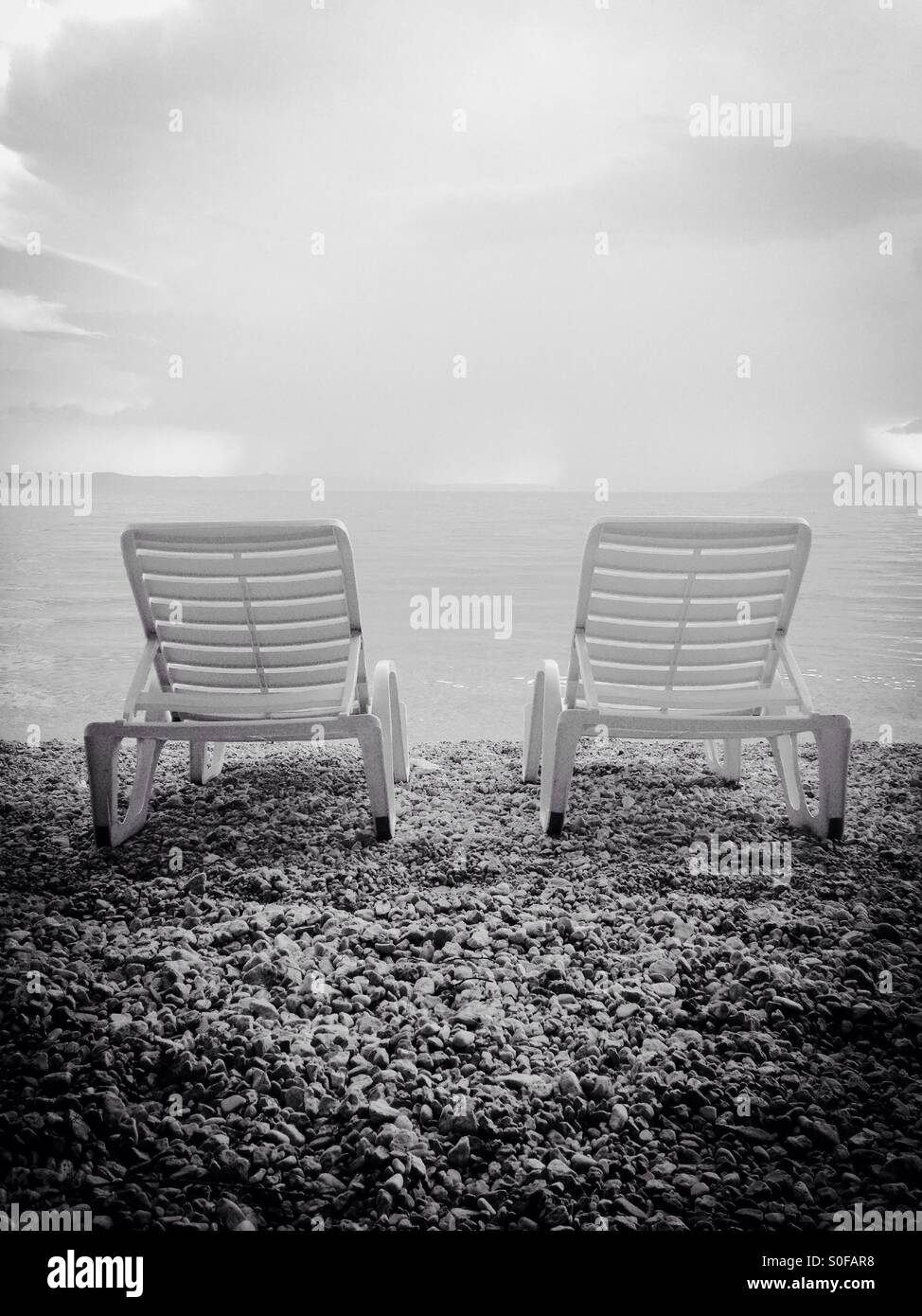 Due sedie a sdraio sulla spiaggia con cielo molto nuvoloso in bianco e nero Foto Stock