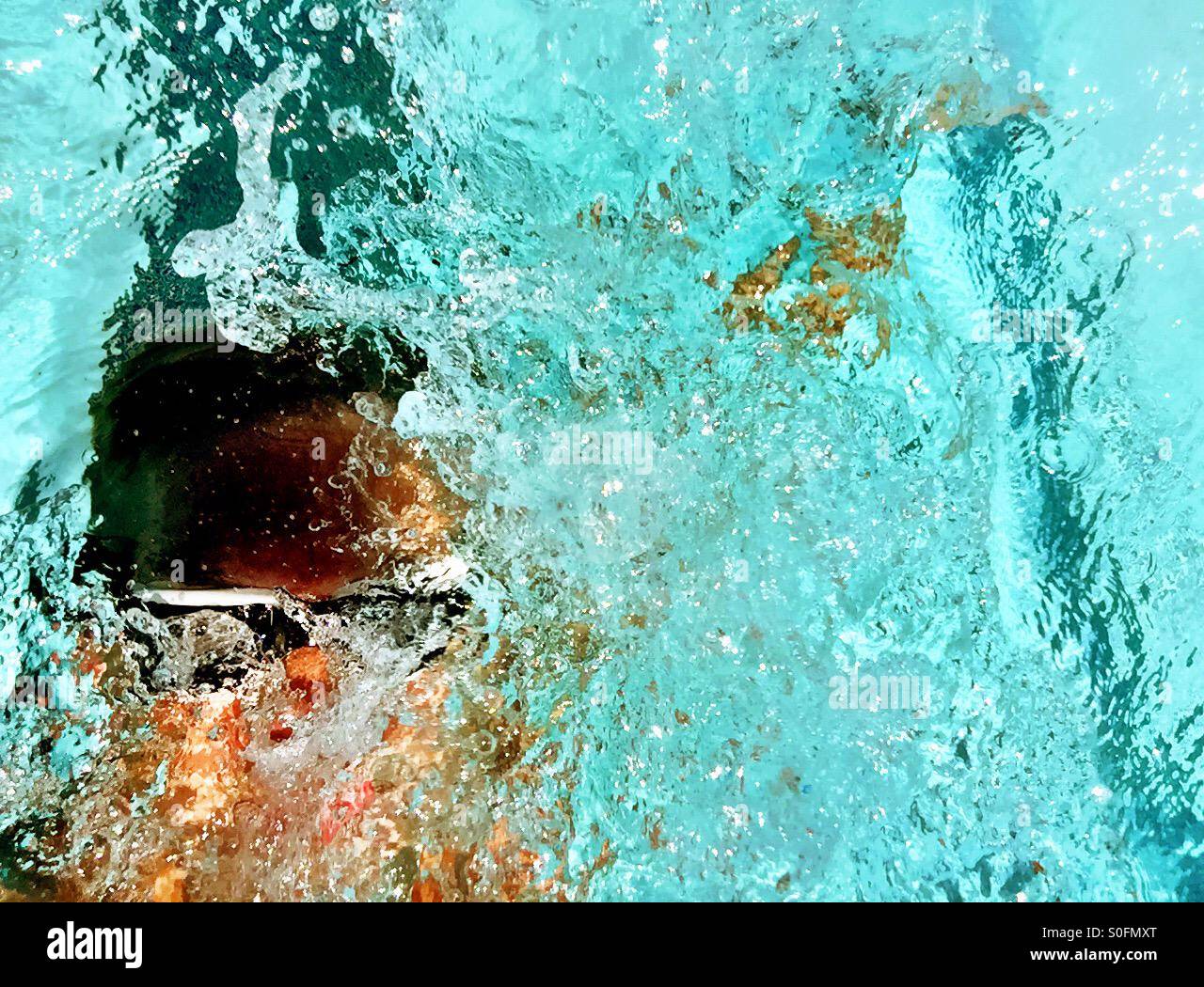 Primo piano sopra l uomo nuoto concorrenza dorso in una piscina esterna. Sun luccicante attraverso la riattivazione e spruzzi d'acqua. Foto Stock