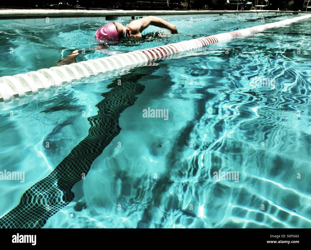 La femmina del nuotatore. Donna nuoto concorrenza freestyle crawl australiano in rosa swim cap. Vista dalla corsia adiacente. Foto Stock