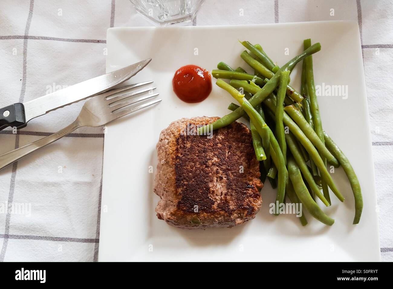 Fagioli verdi e burger bistecca con ketchup su un tavolo bianco panno con posate Foto Stock