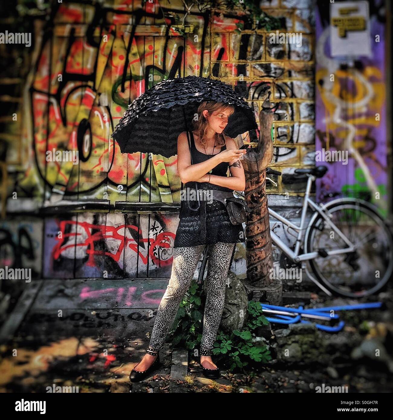 La donna in attesa sotto un ombrellone di fronte a un muro di graffiti - Immagine stock catturata con smartphone