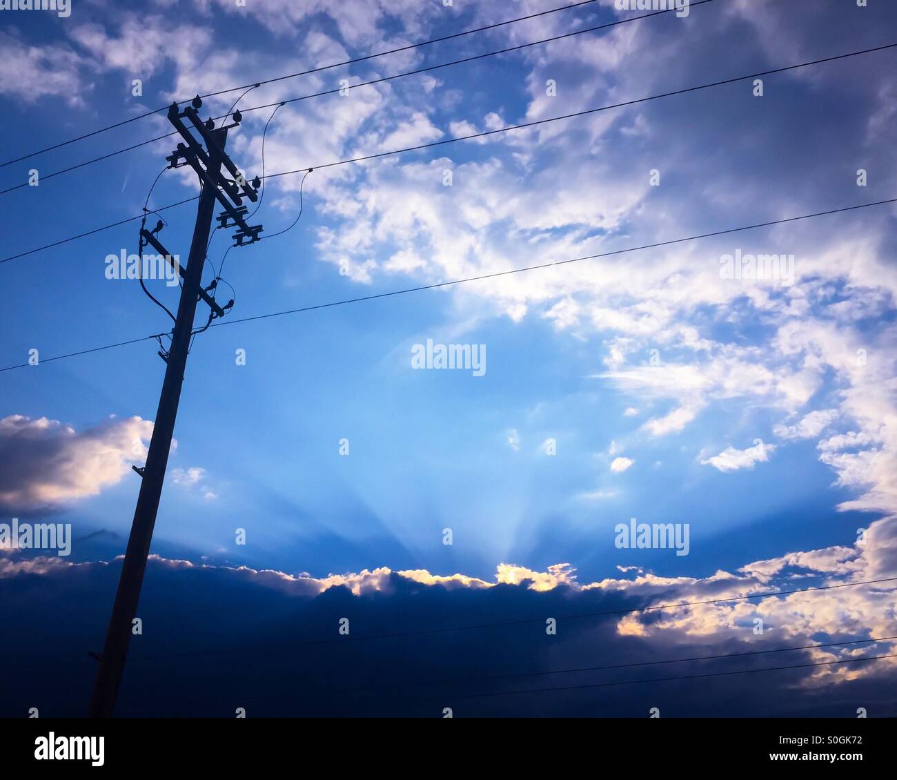 Polo elettrico contro il cielo blu. Il tardo pomeriggio i raggi di sole sono peaking attraverso le nuvole basse in background. Foto Stock