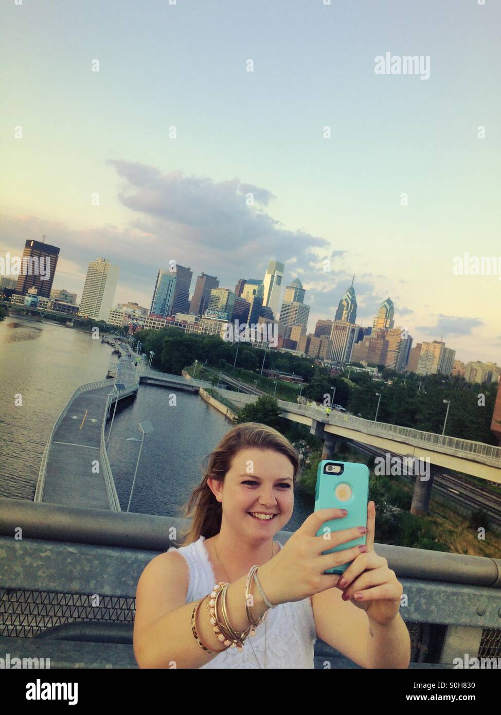 Ragazza con Schuylkill River Boardwalk e dello skyline di Philadelphia in background tenendo selfie Foto Stock