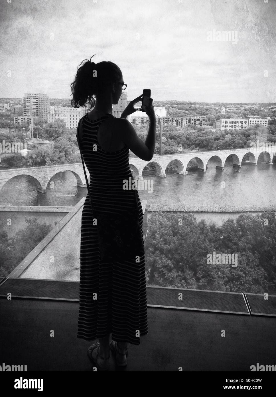 Una donna di scattare una foto della pietra il ponte di arco in Minneapolis, da una finestra del Guthrie Theater. Foto Stock