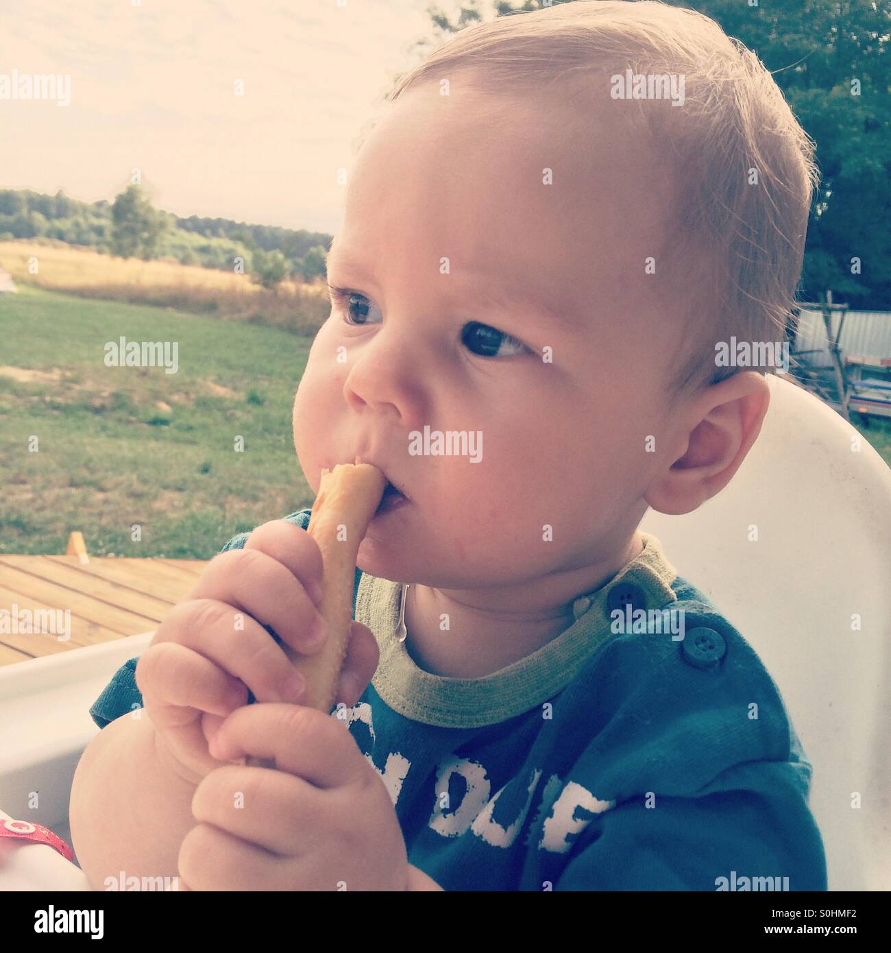 Baby boy di mangiare un pezzo di pane all'esterno Foto Stock