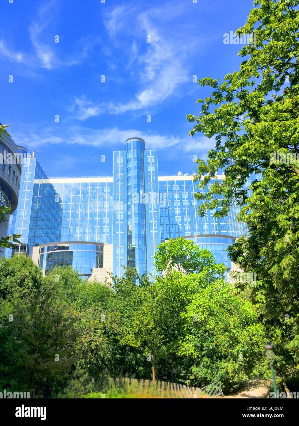 Edifici del Parlamento europeo dietro alberi verdi sotto un cielo blu, Bruxelles, Belgio - Immagine stock catturata con smartphone