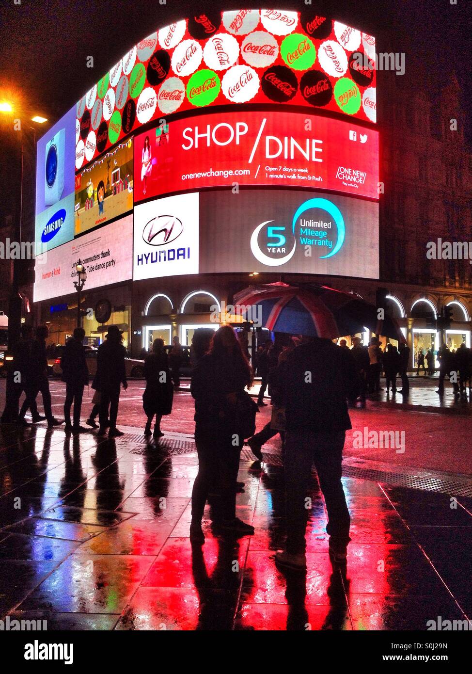 Un turista con una Unione Jack ombrello sorge in una notte piovosa tempo Piccadilly Circus a Londra Foto Stock
