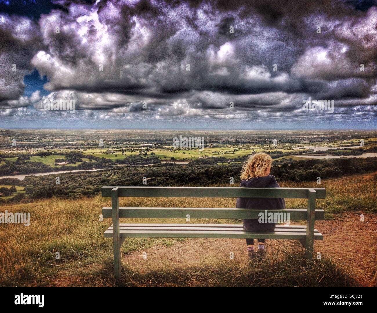 Ragazza giovane da solo su un banco di lavoro guardando avvicinando nuvole di tempesta Foto Stock