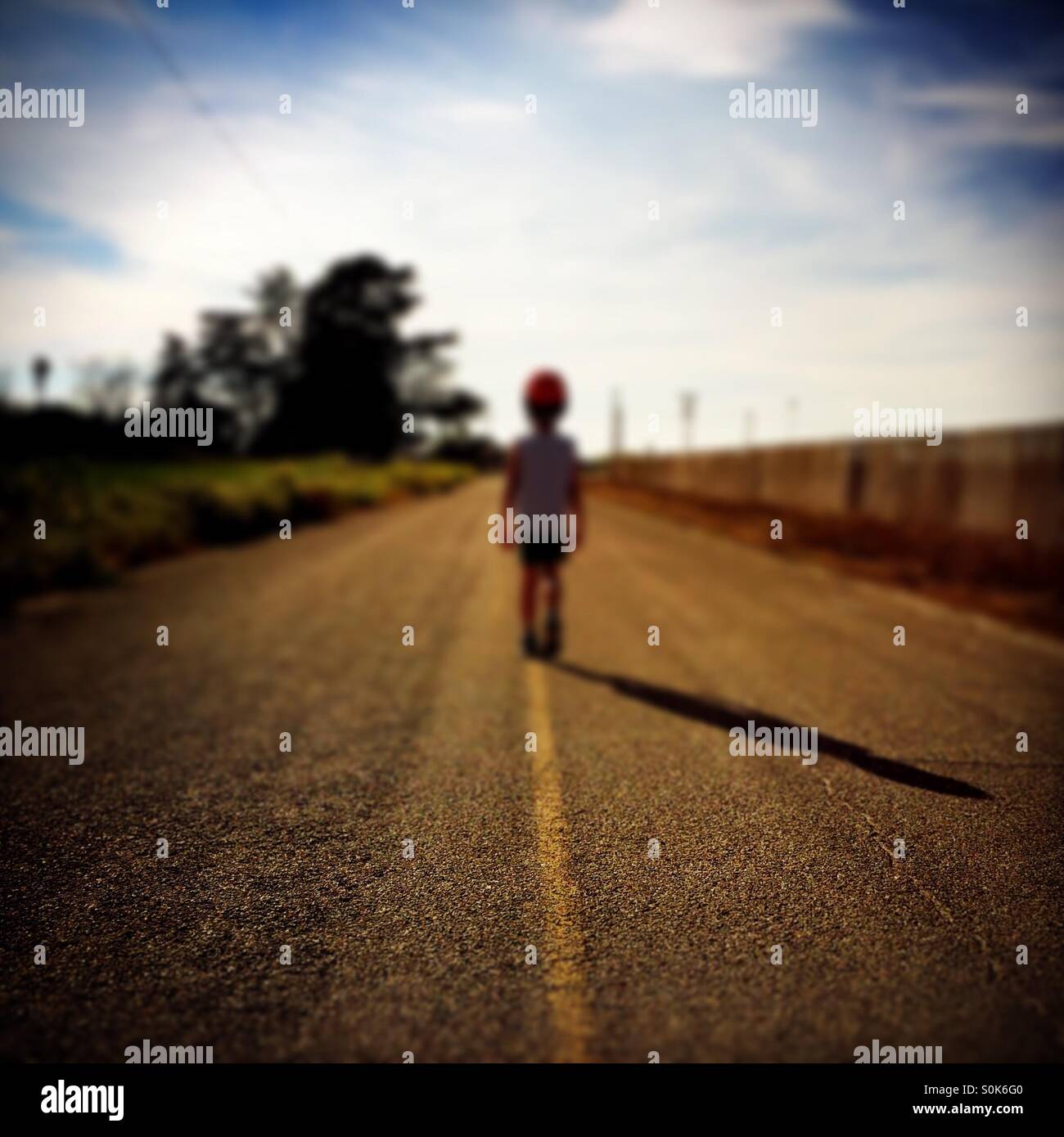 Un ragazzo di 7 anni si erge nel mezzo di una strada di campagna che indossa il suo casco per bicicletta. Foto Stock