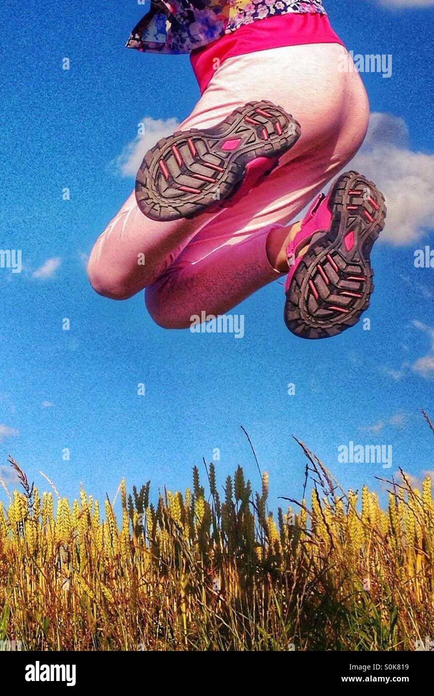 Le gambe della ragazza saltando sopra il campo di grano contro un cielo blu Foto Stock