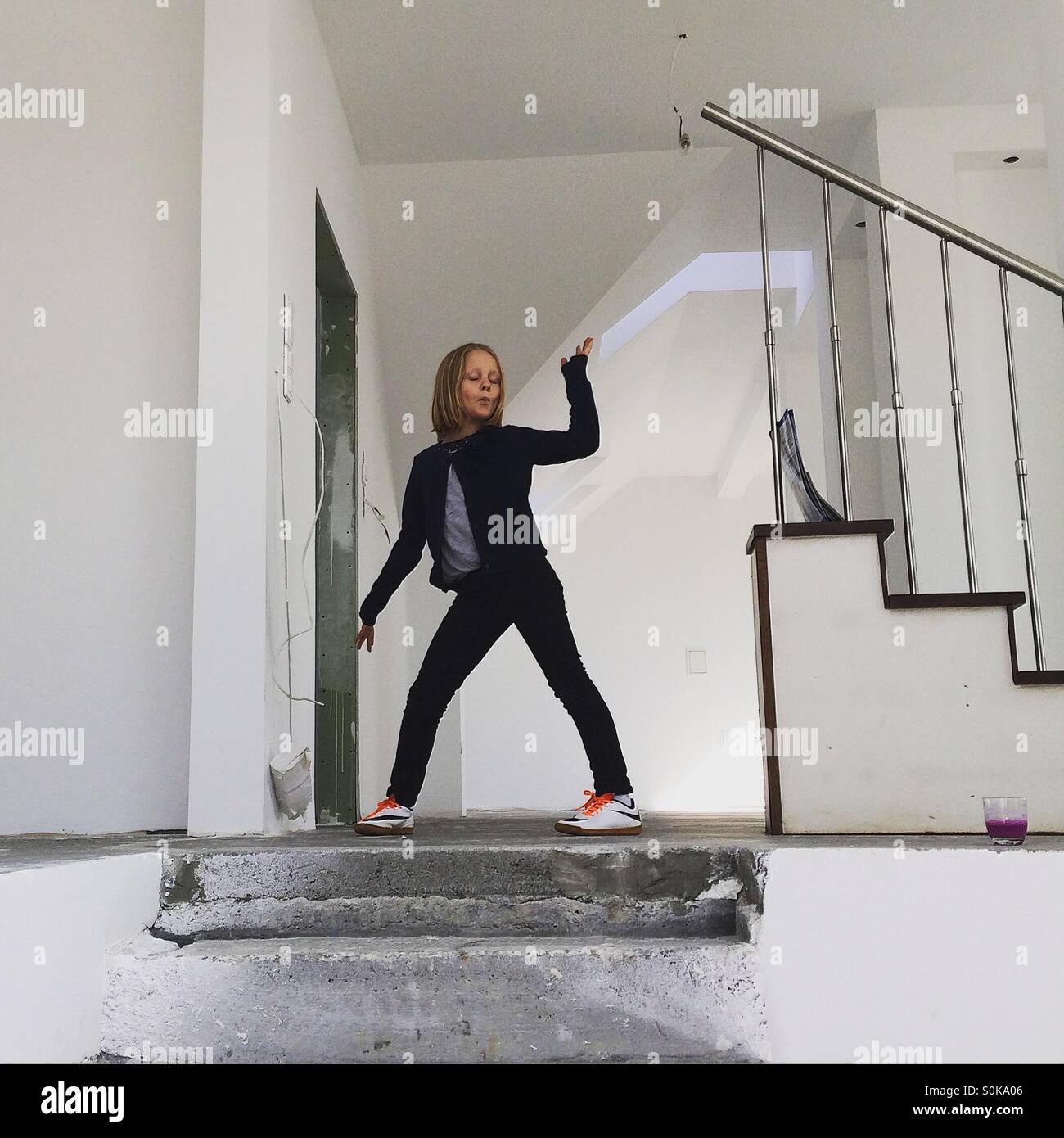 Ragazza rendere divertente pone in piedi in cima alle scale in un vuoto bianco casa nuova Foto Stock