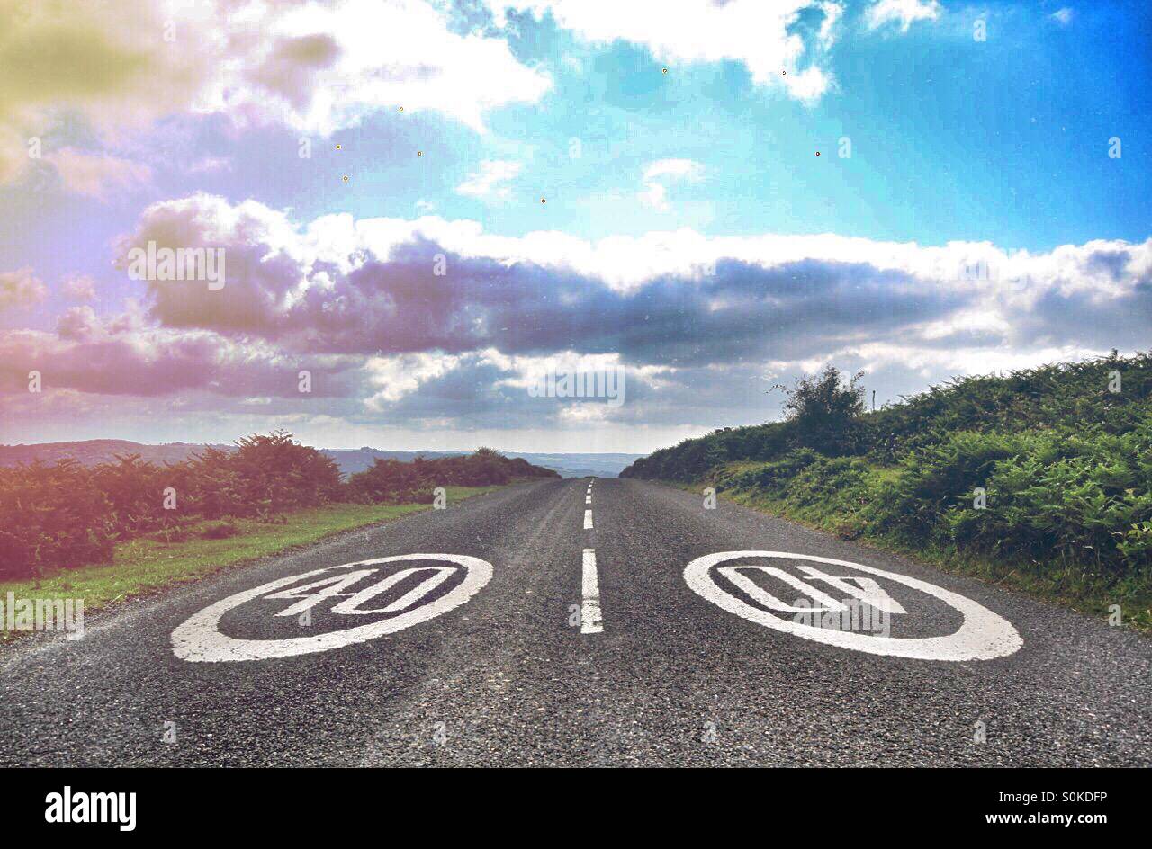 Una strada con 40 miglia per ora i segnali di avvertimento scompare sopra una collina. Un blu cielo nuvoloso sopra e una perdita di luce texture aggiunto. Foto Stock