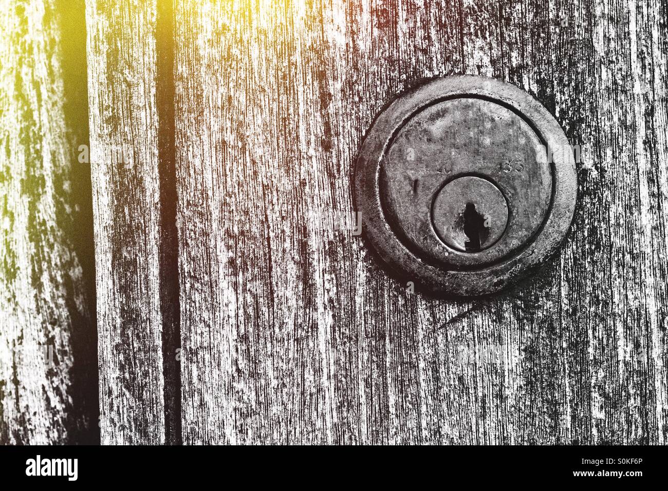 Un vecchio, indossato serratura della porta su un aspetto granuloso superficie di legno con una perdita di luce nella parte superiore sinistra dell'immagine. Foto Stock