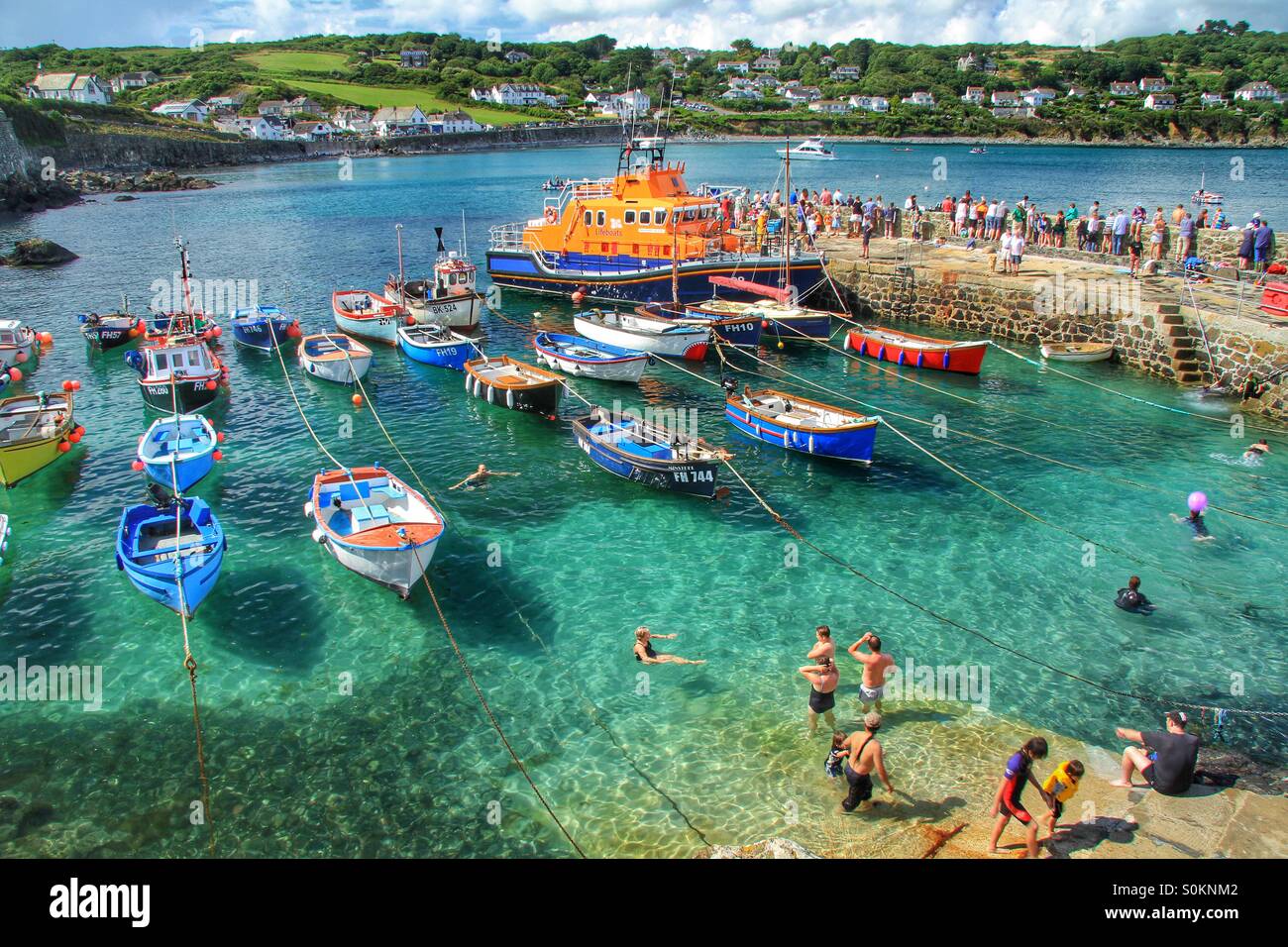 Un occupato Cornish harbour durante una famiglia giornata di divertimento con il RNLI scialuppa di salvataggio di presenze. Una vacanza scena di paesaggio con un sacco di turisti nuotare e divertirsi. Foto Stock