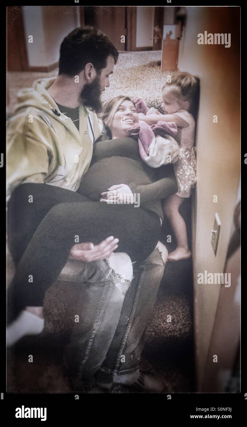 Crescente famiglia, marito mantiene la sua moglie incinta con la loro bambina di due anni sulle scale Foto Stock
