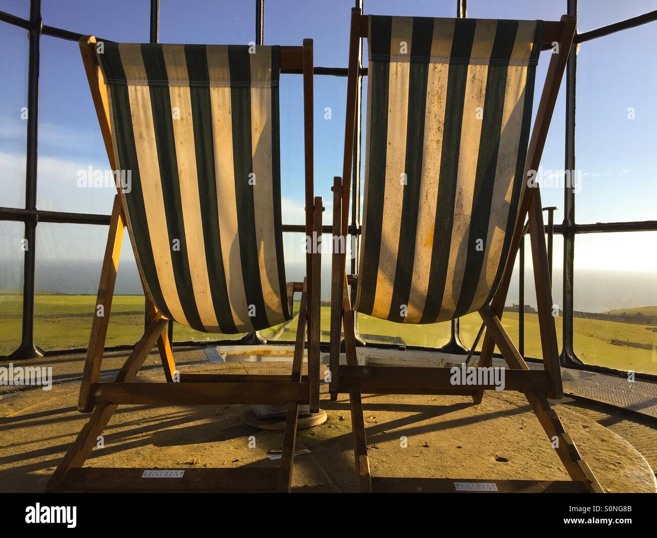 Guardando al mare, sedie a sdraio alla parte superiore di un vecchio faro Foto Stock