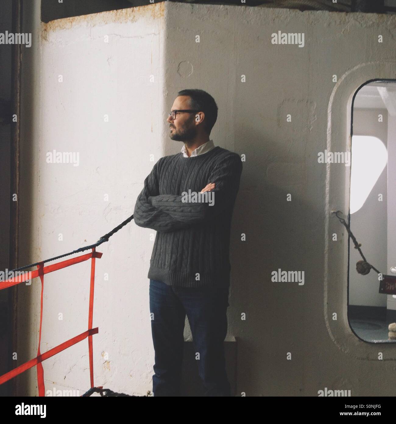 Uomo in cavo grigio maglione maglia con le braccia incrociate in piedi sul traghetto Foto Stock