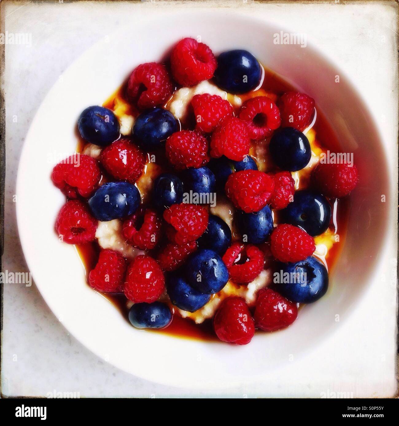 Porridge con mirtilli e lamponi e sciroppo d'acero per la prima colazione - Immagine stock catturata con smartphone