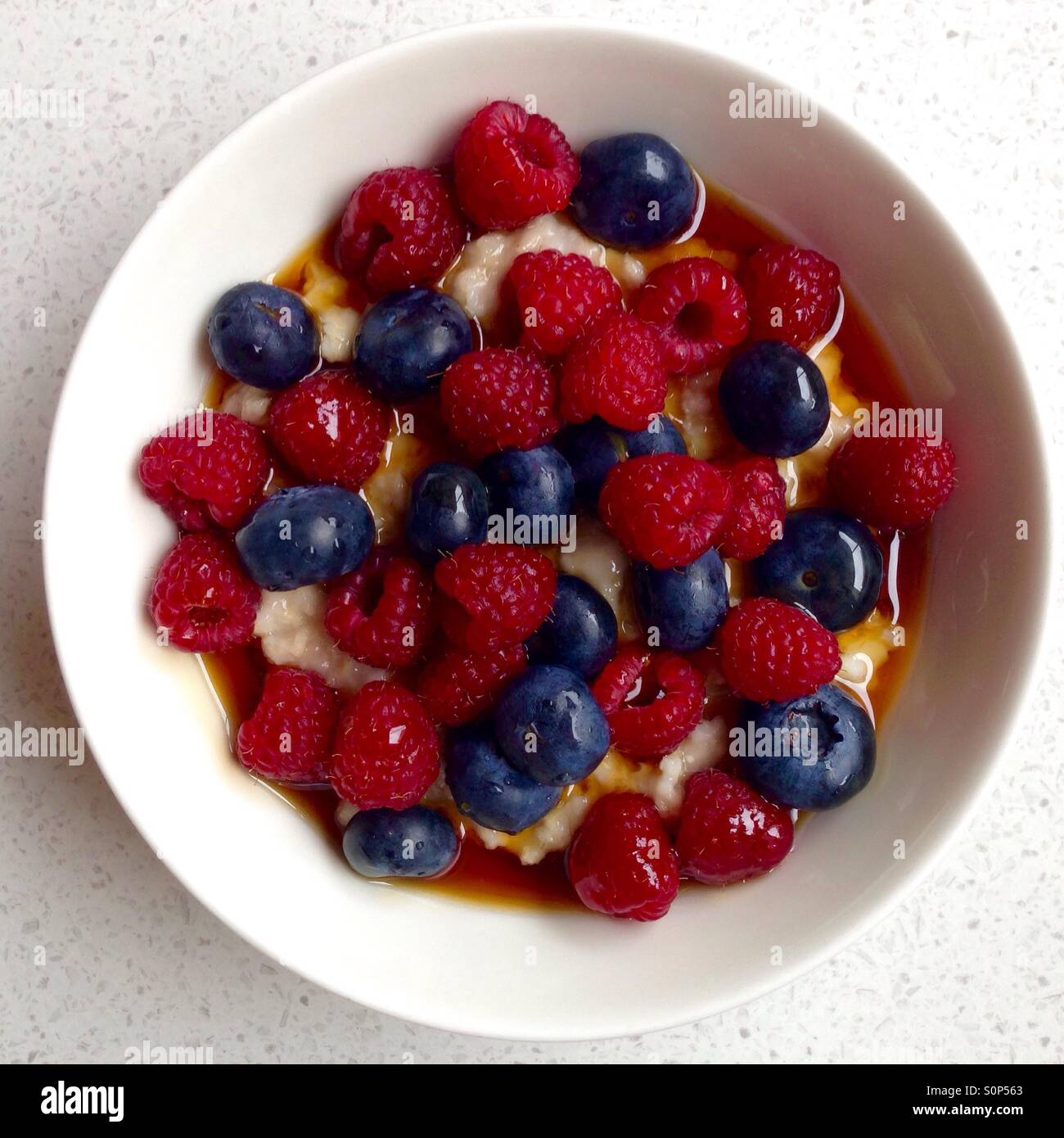 Ciotola di porridge con mirtilli e lamponi e sciroppo d'acero per la prima colazione - Immagine stock catturata con smartphone