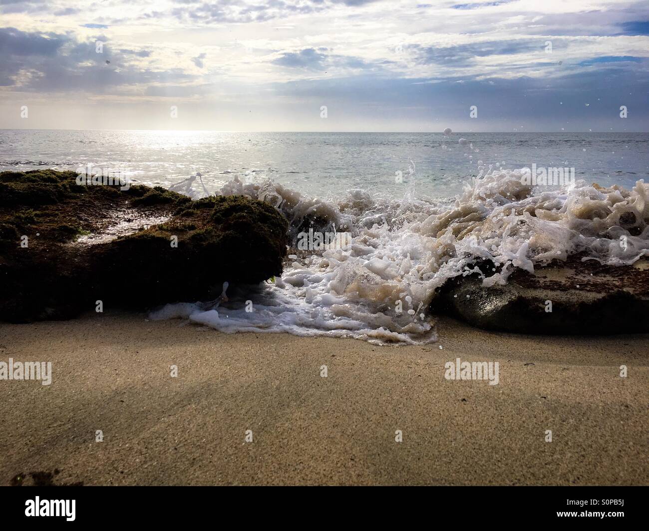 Acqua di mare impetuoso attraverso lo spazio tra due rocce su di una spiaggia di sabbia - Immagine stock catturata con smartphone