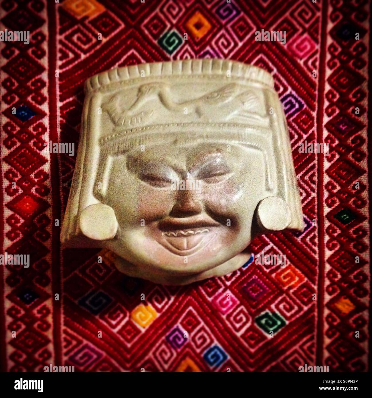 Un folk art di Olmec volto sorridente sulla parte superiore di un Oaxacan tessitura geometrica decora una casa di città del Messico, Messico - Immagine stock catturata con smartphone