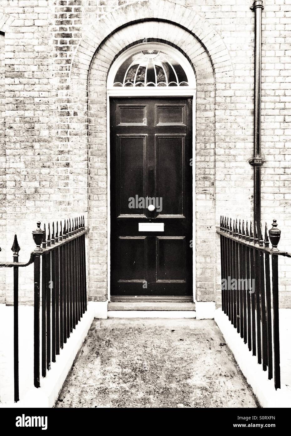 Parte anteriore nera porta con ringhiere in ferro in un edificio in mattoni - Immagine stock catturata con smartphone