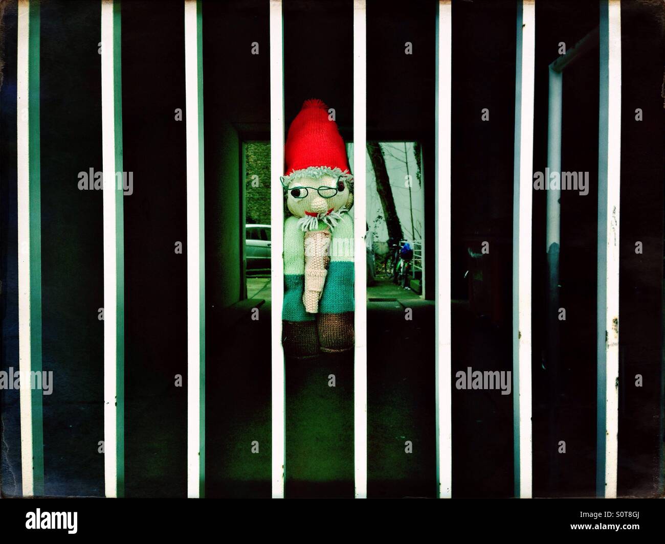 Perso nana giocattolo morbido schiacciato tra le barre di un cancello bianco al fine di trovare più facilmente - Immagine stock catturata con smartphone