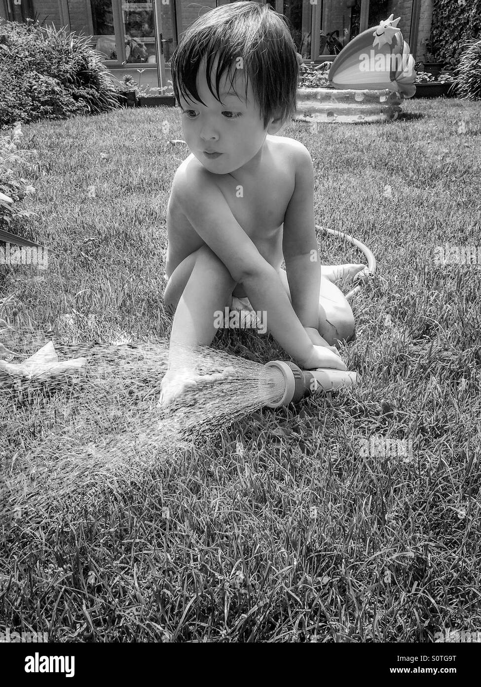 Little Boy giocando con un tubo flessibile da giardino Foto Stock