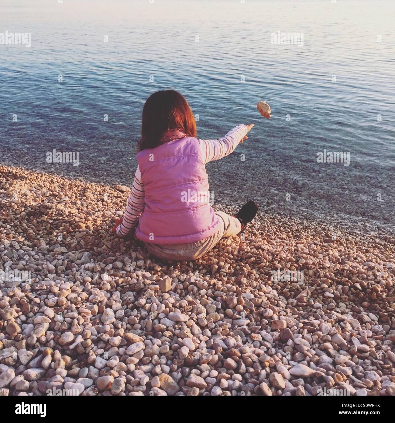 Bambina sulla spiaggia che lanciano pietre nel mare Foto Stock
