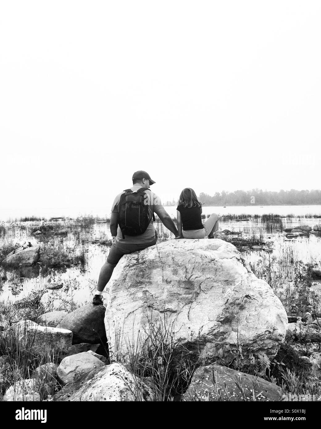 Padre e figlia seduto su una roccia in riva al lago. Foto Stock